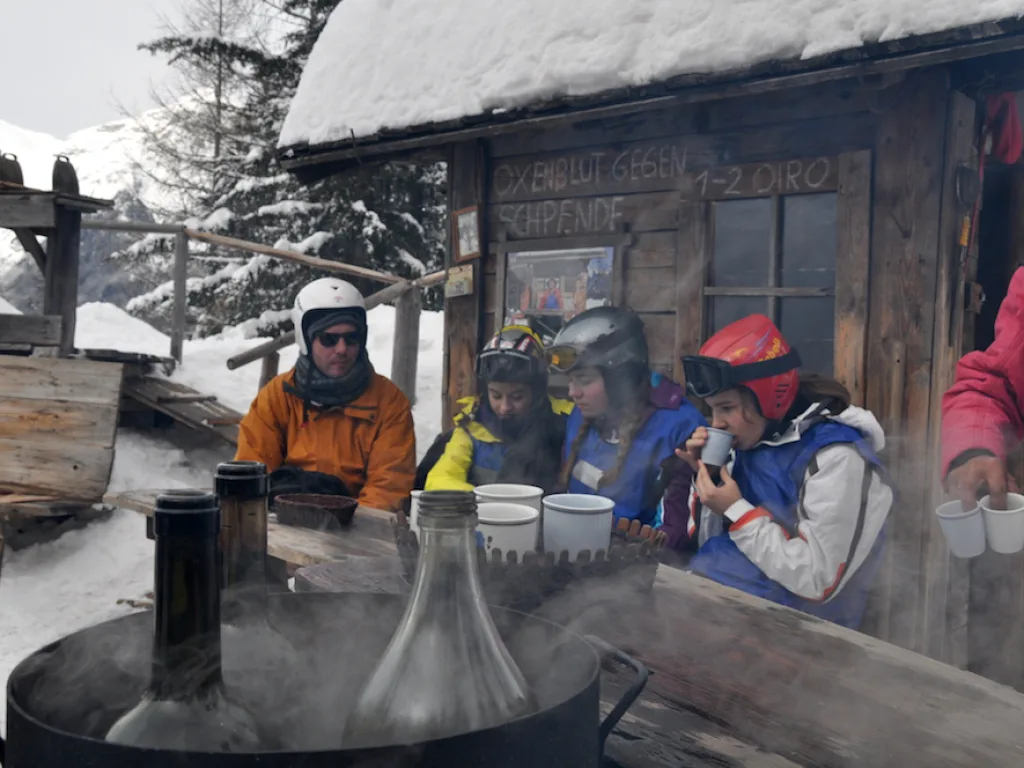 Personen stehen an einer Hütte, davor dampft ein Kessel.